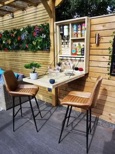 two chairs sitting at a table in front of a wooden wall with plants growing on it