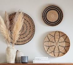 three woven baskets are hanging on the wall above a mantel with a vase and some dried grass in it