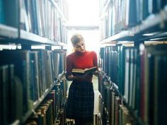 a woman standing in the middle of a library holding a book and looking at it