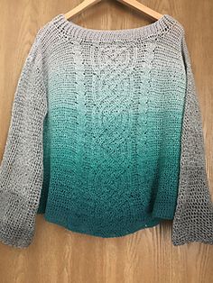 a green and grey sweater hanging on a wooden hanger next to a wood floor