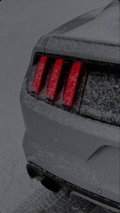 the rear end of a car covered in snow with red brake lights on it's taillights