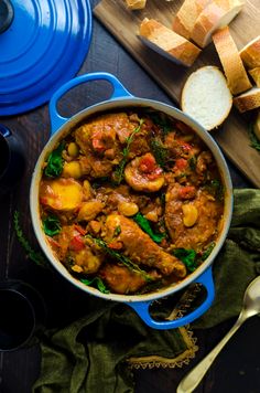 a blue pot filled with meat and vegetables next to bread