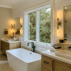 a large white bath tub sitting next to two sinks in a bathroom under a window