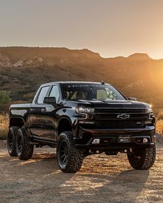 a black truck is parked in front of a mountain range at sunset with the sun behind it