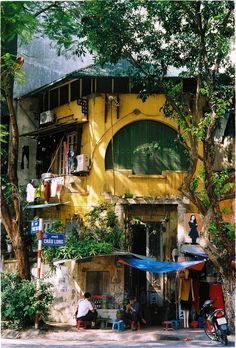 a yellow building with green shutters and people sitting outside