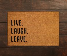 a door mat with the words live laugh leave on it against a wooden background that says live laugh leave