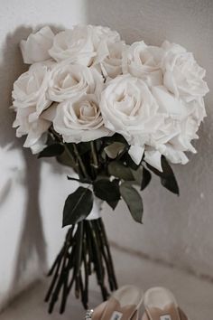 a bouquet of white roses sitting on top of a table next to two pairs of shoes