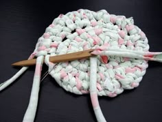 a crocheted dishcloth with pink and white yarn on it, next to a pair of knitting needles