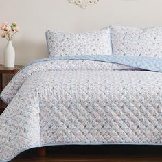 a blue and white quilted bedspread on a bed with flowers in vase