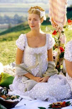 two women sitting next to each other on top of a grass covered field with flowers