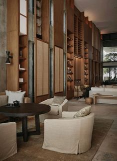 a living room filled with lots of furniture next to a tall wooden wall covered in bookshelves