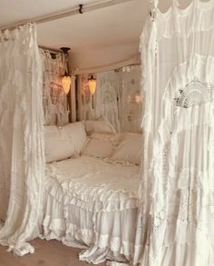 a white bed sitting in a bedroom next to a window with curtains on the sides