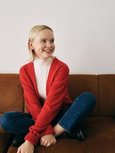 a woman sitting on top of a brown couch next to a white wall and smiling