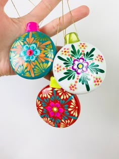 three colorful ornaments hanging from strings in someone's hand