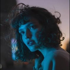 a close up of a person with curly hair looking at the camera and staring into the distance