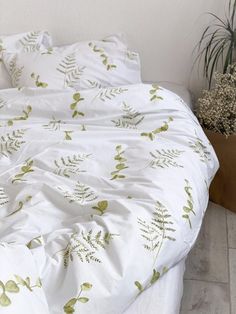 an unmade bed with white sheets and green plants on the comforter, next to potted plant