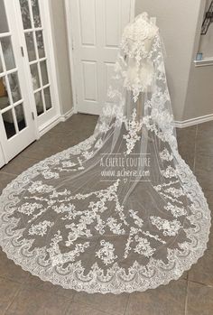 a white wedding veil with flowers on the bottom and lace at the bottom, sitting in front of a door