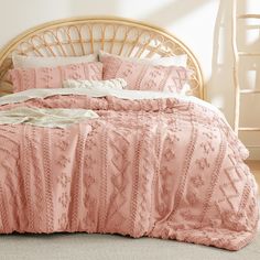 a bed with pink comforter and pillows on top of it in front of a wicker headboard