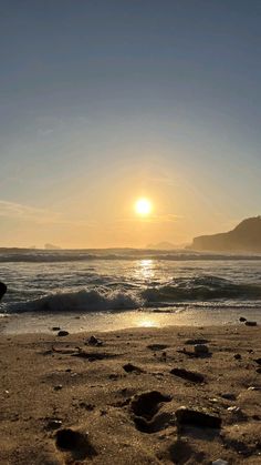 the sun is setting at the beach with footprints in the sand