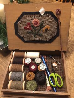 a wooden box filled with lots of different types of yarn and scissors on top of a table