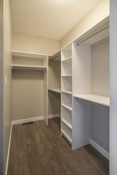 an empty walk in closet with white shelving and wood flooring on the side