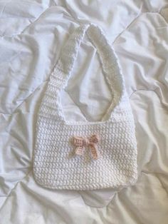 a crocheted white purse with a bow on the side laying on a bed