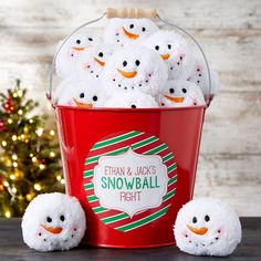 a red bucket filled with snowballs sitting on top of a table next to a christmas tree