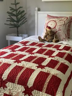 a teddy bear sitting on top of a red and white quilt