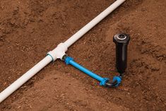 a white and blue pipe laying on top of dirt next to a black plastic spigot