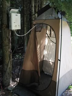 a tent is set up in the woods with its door open and water hose attached to it