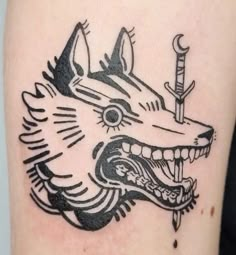 a black and white tattoo of a wolf with a dagger in its mouth, on the arm