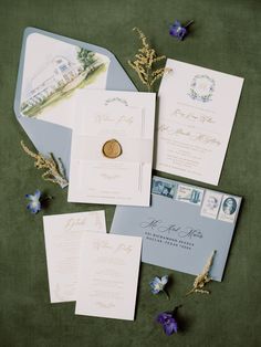 the wedding stationery is laid out on top of each other, with blue flowers and greenery