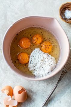 a bowl filled with eggs and cream next to an egg whisk on a table