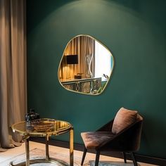 a living room with green walls and a gold mirror on the wall above a glass table