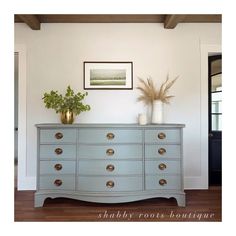 a blue dresser with two vases on top of it and a plant in the middle