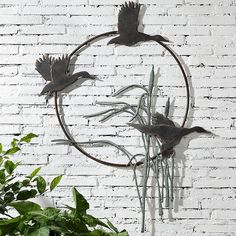 a metal bird sculpture hanging on the side of a white brick wall next to a potted plant