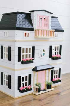 a white doll house with pink doors and windows on top of a hard wood floor