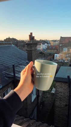 someone holding a coffee cup in their hand on top of a building overlooking the city