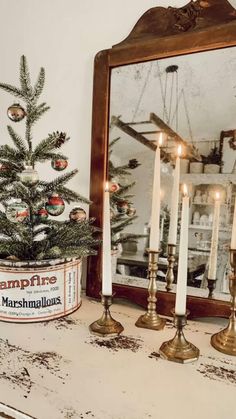 a christmas tree and candles on a mantle with a mirror in the corner behind it