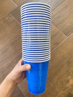 a hand holding a stack of blue and white cups on top of a wooden floor