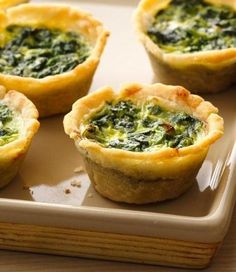 mini quiches filled with spinach and cheese on a tray next to a fork