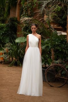 a woman in a white dress standing next to some trees and plants on the ground