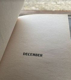 an open book with the word december written on it, sitting next to a window