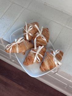 four croissants wrapped in white ribbon on a plate next to a window