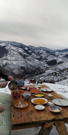 a person sitting at a picnic table with food on it in front of some mountains