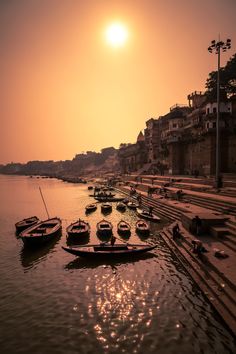 boats are parked on the shore as the sun sets in the sky over some buildings