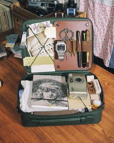 an open suitcase sitting on top of a wooden floor next to a table with other items in it