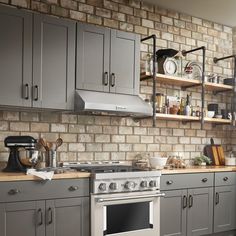 a kitchen with gray cabinets and stainless steel stove top oven in the center, surrounded by open shelving