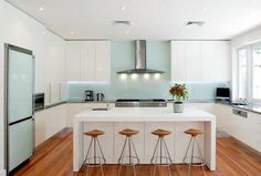 a large kitchen with white cabinets and wooden flooring, along with three bar stools