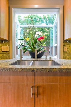 a kitchen sink sitting under a window next to a counter top with flowers in it